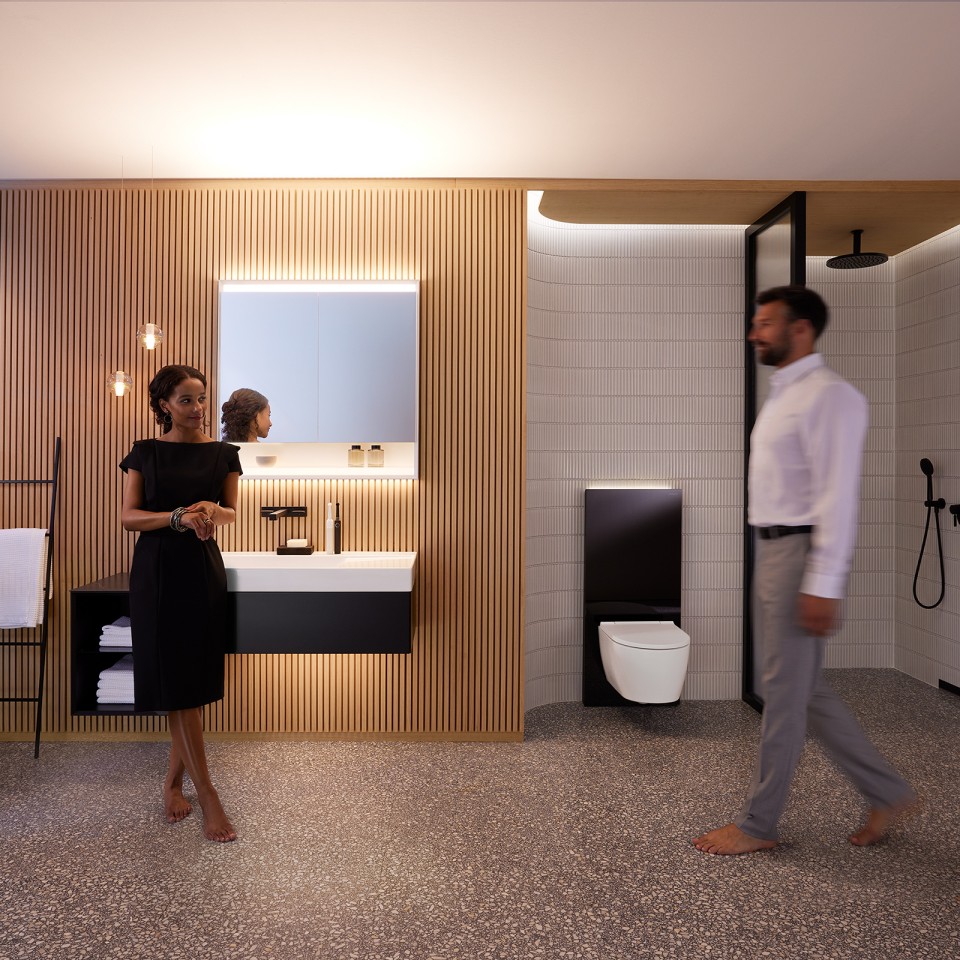 Moški in ženska v popolnoma osvetljeni kopalnici s kopalniškim pohištvom Geberit ONE in keramičnimi izdelki (© Geberit)
