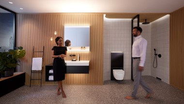 Moški in ženska v popolnoma osvetljeni kopalnici s kopalniškim pohištvom Geberit ONE in keramičnimi napravami (© Geberit)