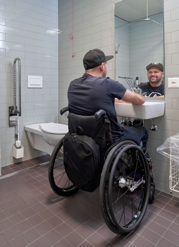 Peter Roos v invalidskem vozičku ob umivalniku v kopalnici brez ovir (© Ben Huggler)