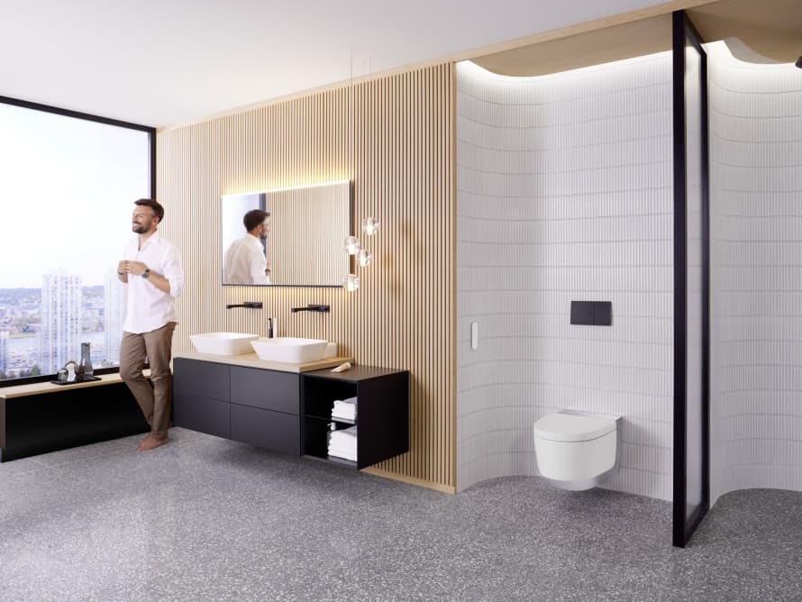 Oseba v veliki kopalnici s temnim pohištvom in Geberit AquaClean tuš WC-jem Oseba v veliki kopalnici s temnim pohištvom in Geberit AquaClean tuš WC-jem